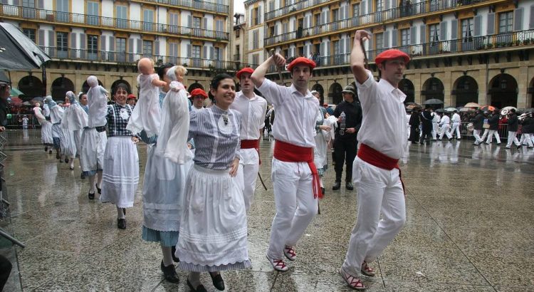 A photo of basque people dressed in traditional clothes and dancing on a city square.