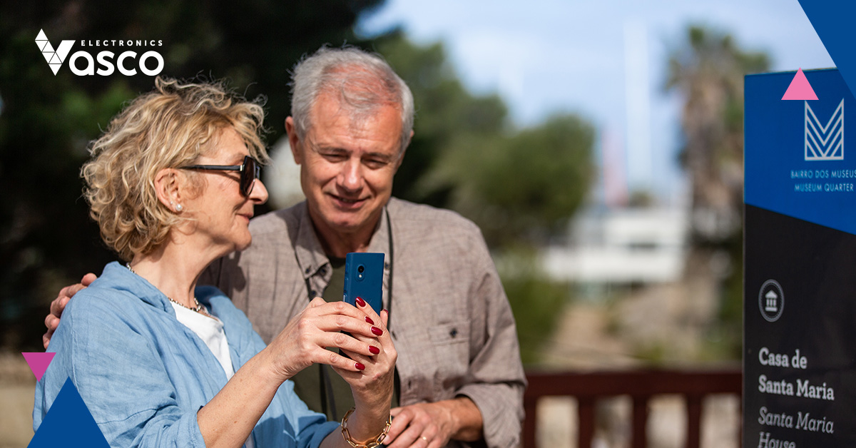 An elderly couple translates text from a message board in a foreign language with the help of a VE device.