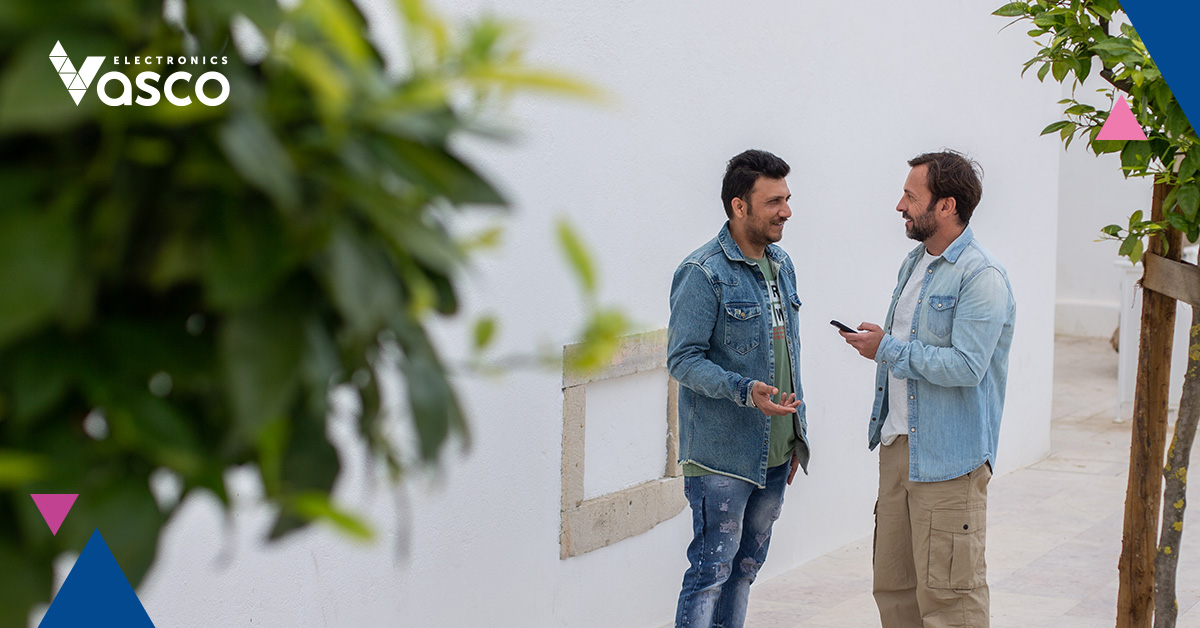 Two men talk against a backdrop of historic walls, using a VE device