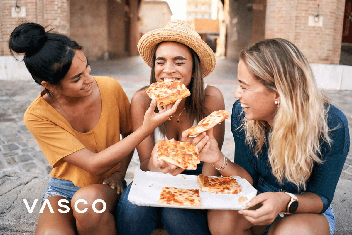 Friends eating pizza on the street.