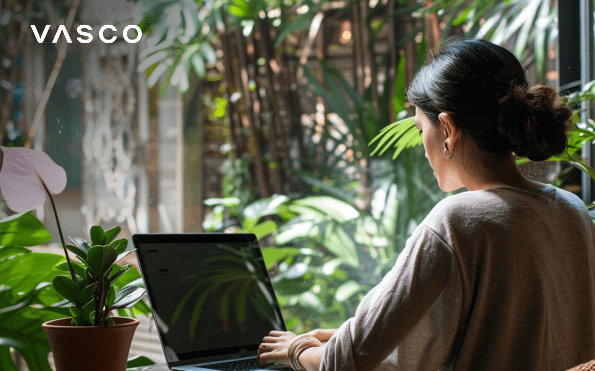 A woman is working on her laptop among trees and plants.