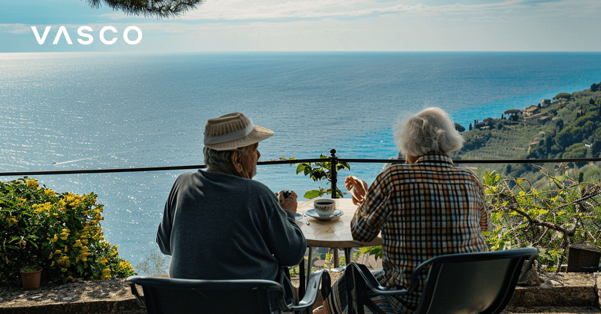 An elderly couple having coffee on the balcony overlooking the sea.