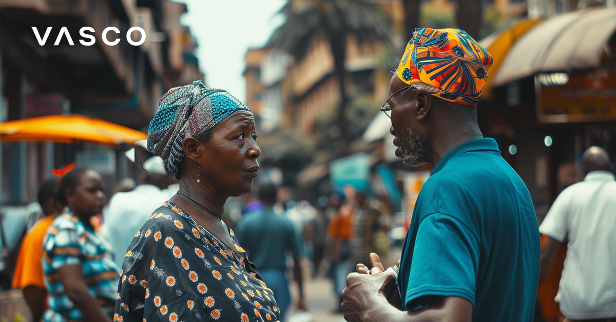 An elderly man and woman having a conversation on a busy street with colorful clothing and people in the background.