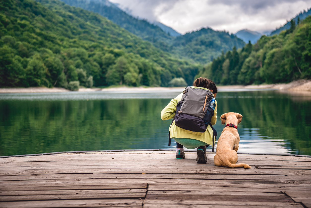 woman standing by a lake with her dog